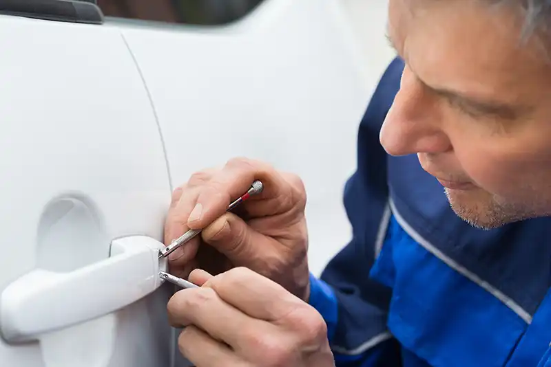 A locksmith is working on a car door lock with tools.